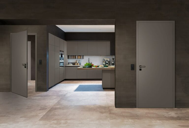 The picture shows two modern interior doors in a room with a minimalist design. Both doors are kept in a simple grey tone and have smooth surfaces with no visible decorations. The doors match the colour of the walls and floor, giving the room a harmonious and uniform appearance.